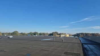 Overzicht van een groot plat dak waarbij meerdere zwakke plekken bijdragen aan een structureel lekkageprobleem.