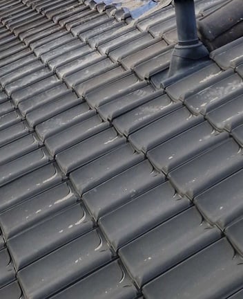 Ernstig verweerde dakpannen met mosgroei en materiaalverlies, waarbij de waterkerende functie lokaal is aangetast.